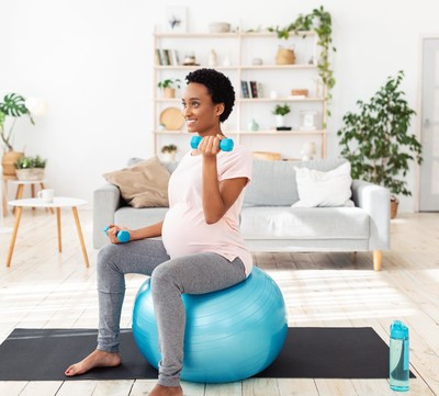 Pregnant woman of color looking happy as she sits on a fitness ball, lifting weights